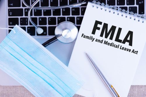 FMLA Family Medical Leave Act, the text is written in a notebook, next to a pen, a disposable medical mask and a laptop on a linen background - fmla vs ada concept