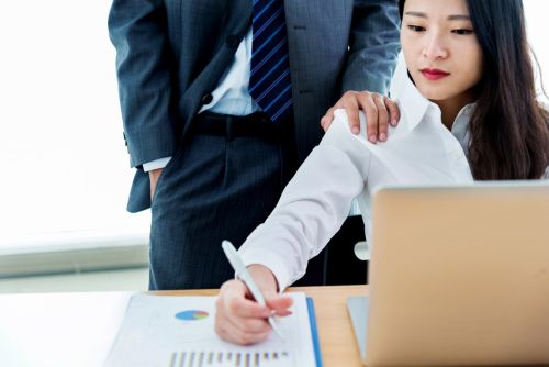 Man looking over the shoulder at his female colleague work - filing sexual harassment claim concept