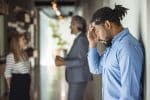 Male African American office worker looking distressed in the foreground as business man talks to business woman in the background - witnessing discrimination concept
